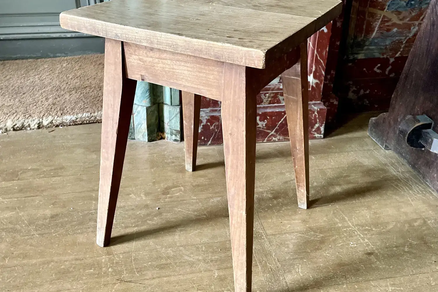 A small, plain wooden stool with straight legs on a wooden floor