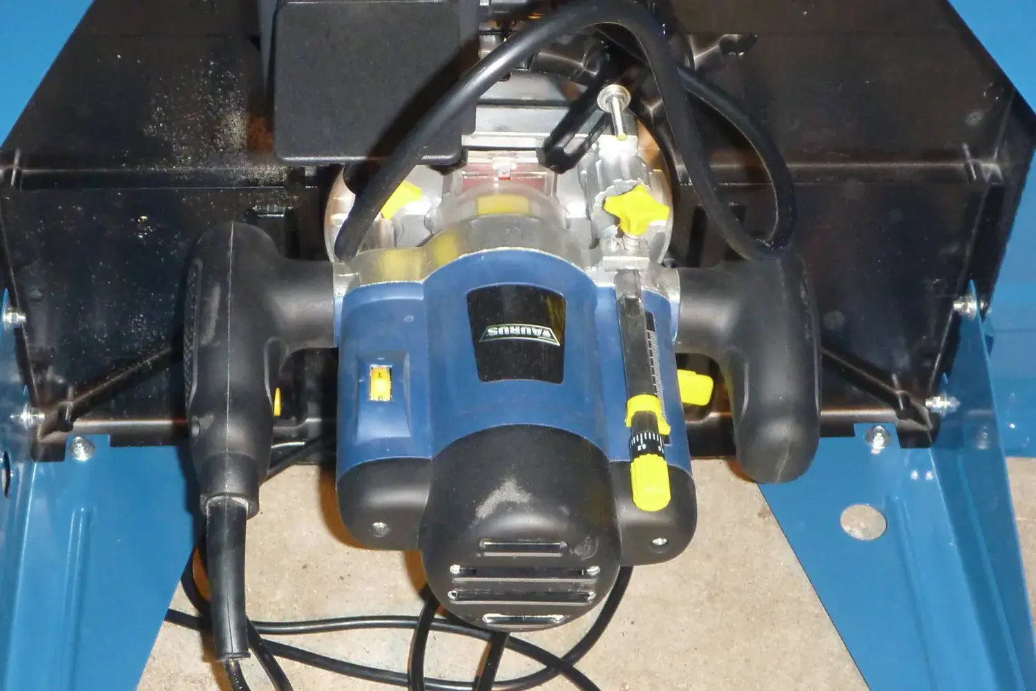 A plunge router mounted upside down under a router table, viewed from below